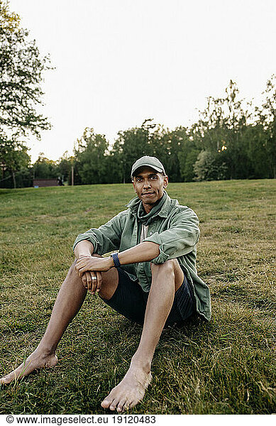 Porträt eines Mannes  der auf einem Spielplatz im Gras sitzt