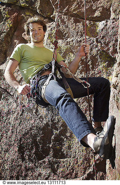 Porträt eines Mannes  der beim Bergsteigen am Sicherheitsgurt hängt