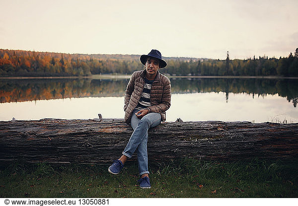 Porträt eines Mannes in voller Länge  der auf einem Baumstamm am See sitzt