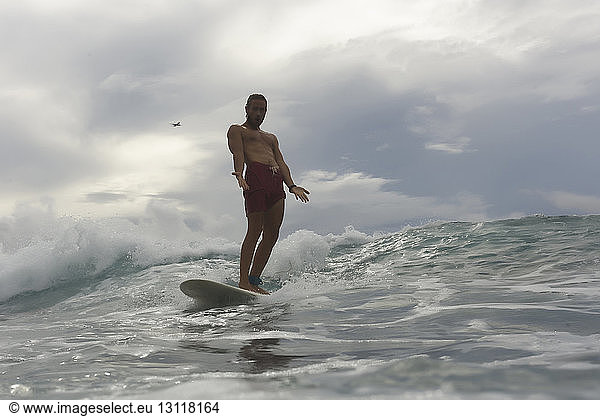Porträt eines Mannes ohne Hemd  der auf dem Meer vor bewölktem Himmel surft