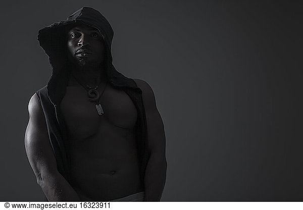 Porträt eines muskulösen Mannes mit Kapuze vor einem dunklen Hintergrund