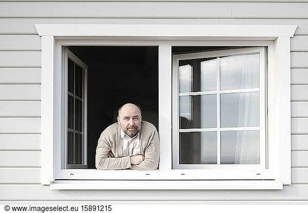 Porträt eines reifen Mannes  der sich aus dem Fenster seines Hauses lehnt