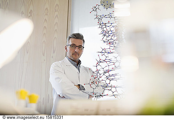 Porträt eines selbstbewussten  ernsten männlichen Lehrers der Naturwissenschaften  der hinter einer Molekularstruktur im Klassenzimmer steht