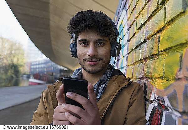 Porträt eines selbstbewussten jungen Mannes  der mit Kopfhörern und mp3-Player Musik hört
