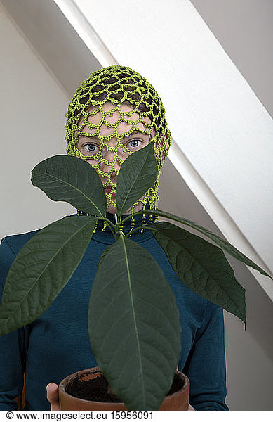 Porträt eines Teenager-Mädchens mit eingetopfter Avocadopflanze mit gehäkelter grüner Kopfbedeckung