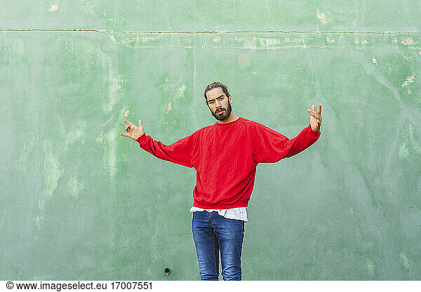 Porträt eines wütenden jungen Mannes mit rotem Sweatshirt vor einer grünen Wand
