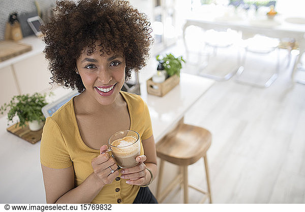 Porträt glückliche junge Frau trinkt Cappuccino in Küche