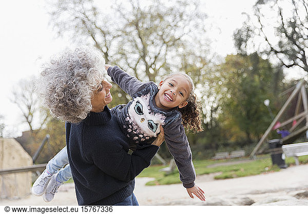Porträt spielerische Großmutter hebt Enkelin auf Spielplatz