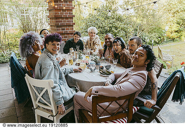 Porträt von glücklichen Freunden aus der LGBTQ-Gemeinschaft  die während einer Dinnerparty im Hinterhof am Esstisch sitzen