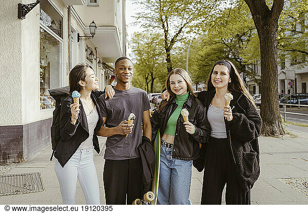Porträt von lächelnden jungen Freunden  die am Straßenrand Eis essen