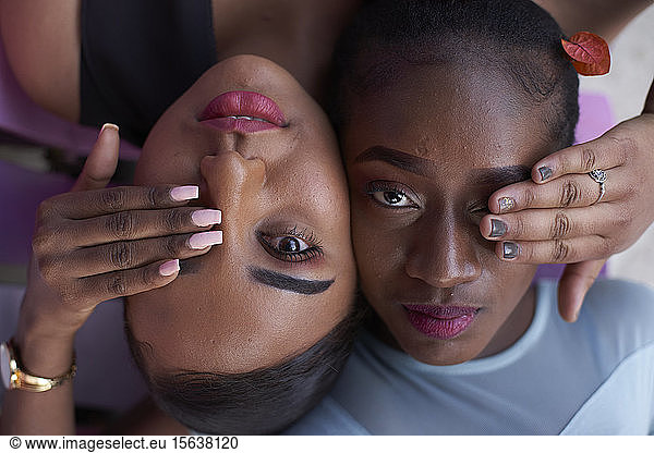 Porträt von zwei jungen Frauen Kopf an Kopf  die mit den Händen die Augen bedecken