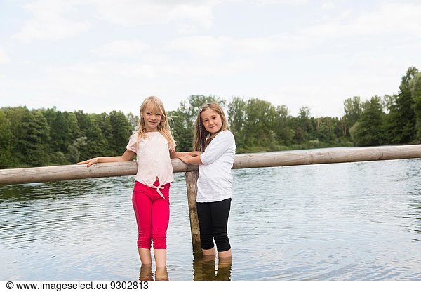 Porträt von zwei Mädchen  die sich am Zaun festhalten  während sie im See paddeln.