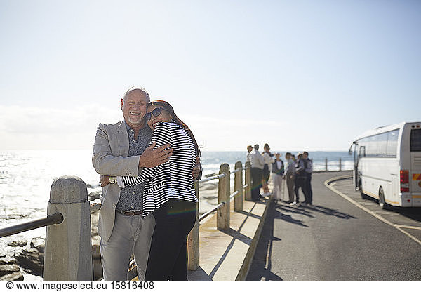 Portrait active senior couple tourists hugging at sunny ocean overlook