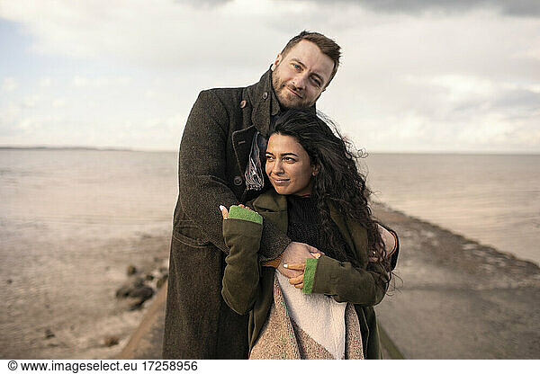 Portrait affectionate couple hugging on winter ocean jetty