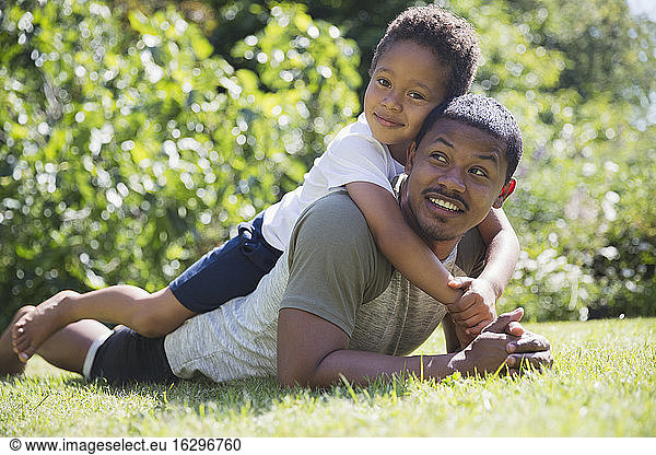 Portrait affectionate father and son laying in sunny summer grass