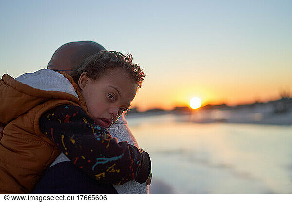 Portrait boy with Down Syndrome on father shoulder on beach at sunset