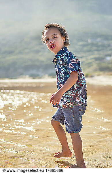 Portrait boy with Down Syndrome wading in ocean on sunny beach