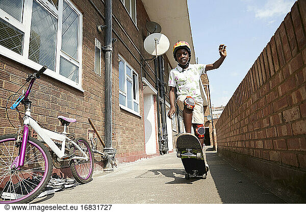 Portrait carefree boy skateboarding in sunny apartment alleyway