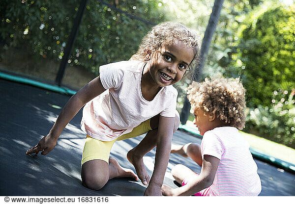 Portrait carefree sisters playing on backyard trampoline