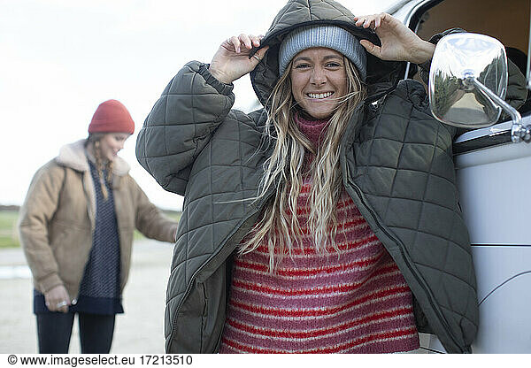 Portrait carefree young woman in hooded jacket at van