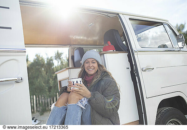 Portrait carefree young woman with coffee in sunny camper van