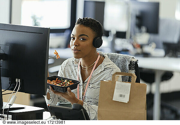 Portrait confident businesswoman eating takeout lunch at office desk