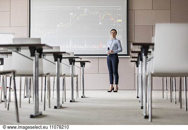 Portrait confident businesswoman with microphone at projection screen with chart in conference room