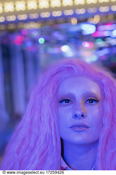 Portrait confident cool woman with pink hair under neon light