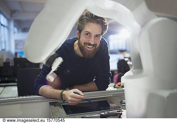 Portrait confident engineer with digital tablet operating robotic arm