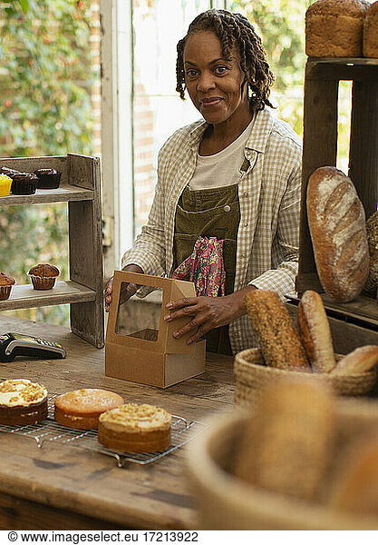 Portrait confident female baker boxing pastries in shop