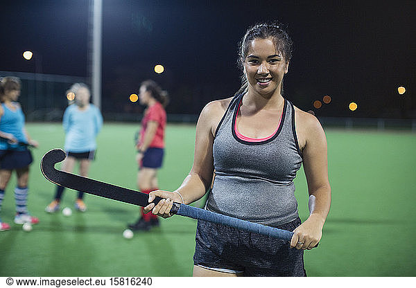 Portrait confident female field hockey player holding hockey stick on field