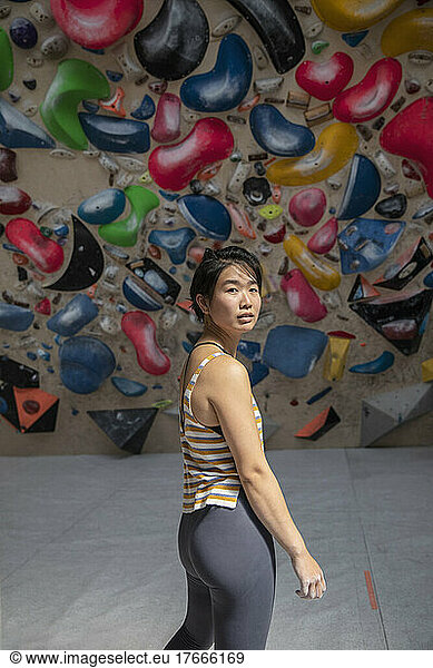 Portrait confident female rock climber standing below rock wall