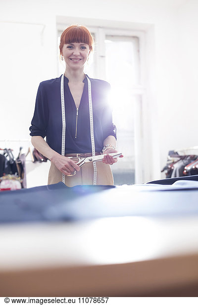 Portrait confident female tailor holding scissors in menswear workshop