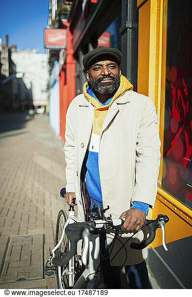 Portrait confident handsome man with. bicycle on sunny sidewalk