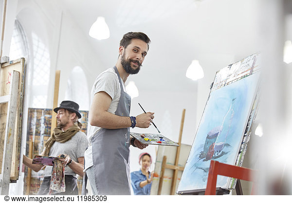 Portrait confident male artist painting with palette in art class studio