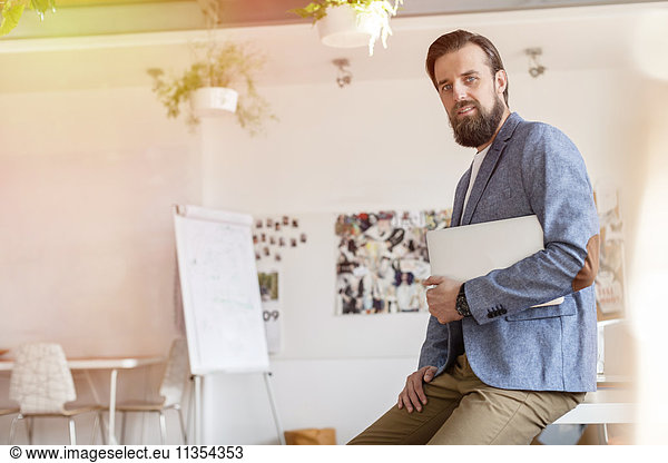 Portrait confident male design professional holding laptop in office