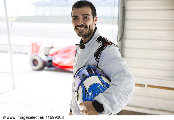Portrait confident male formula one race car driver holding helmet in repair garage