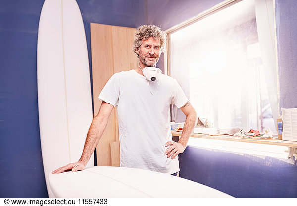 Portrait confident male surfboard designer sanding surfboard in workshop