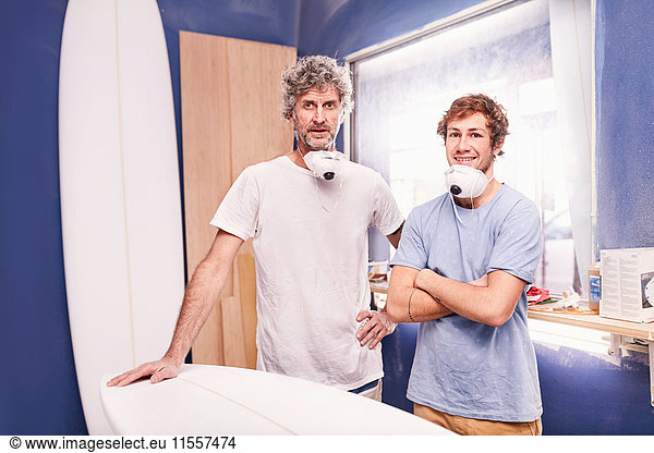 Portrait confident male surfboard designers with protective masks in workshop