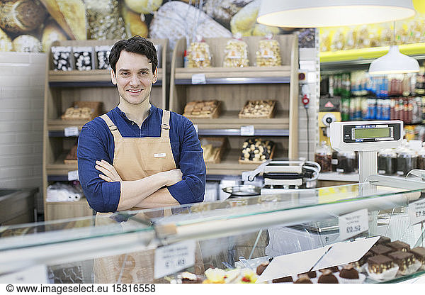 Portrait confident male worker behind bakery display case in supermarket