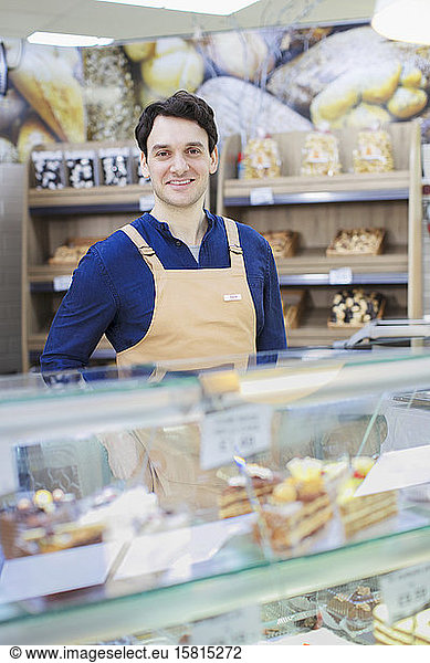 Portrait confident man working at bakery display case in supermarket