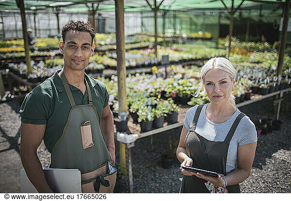 Portrait confident plant nursery owners in sunny greenhouse