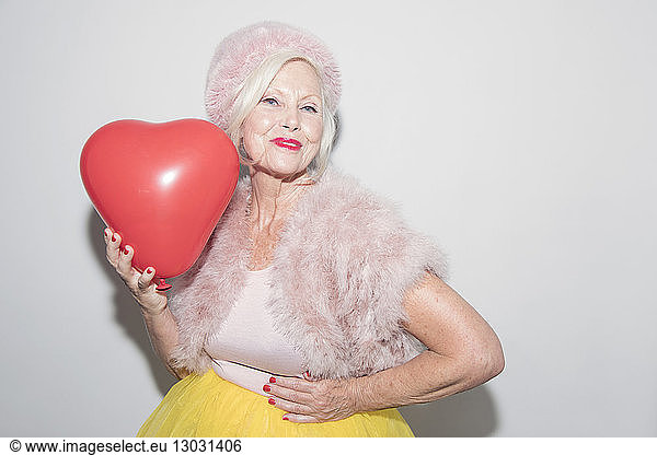 Portrait confident senior woman in fur holding heart-shape balloon