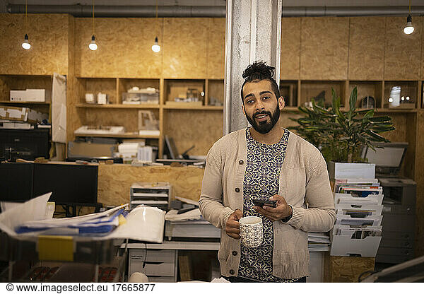 Portrait confident young male designer with coffee and phone