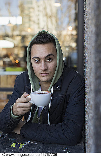 Portrait confident young man in hoody drinking cappuccino