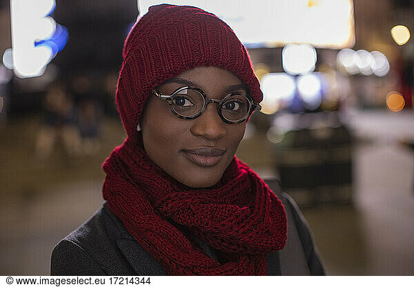 Portrait confident young woman in eyeglasses scarf and hat at night