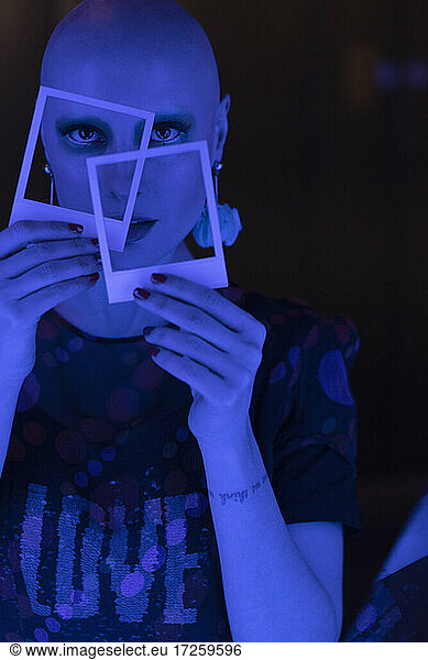 Portrait cool woman with shaved head holding polaroids in blue light