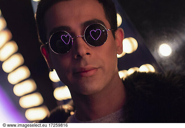 Portrait cool young man with neon heart reflection in sunglasses