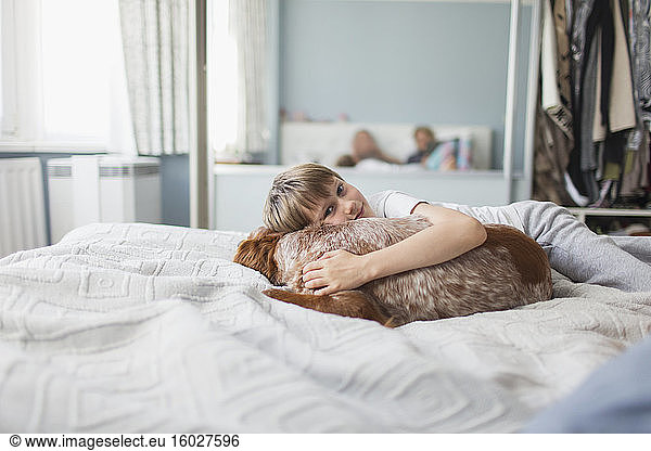 Portrait cute boy cuddling dog on bed