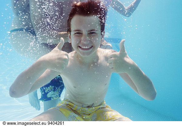 Portrait des Jungen mit Daumen nach oben unter Wasser  Person im Hintergrund